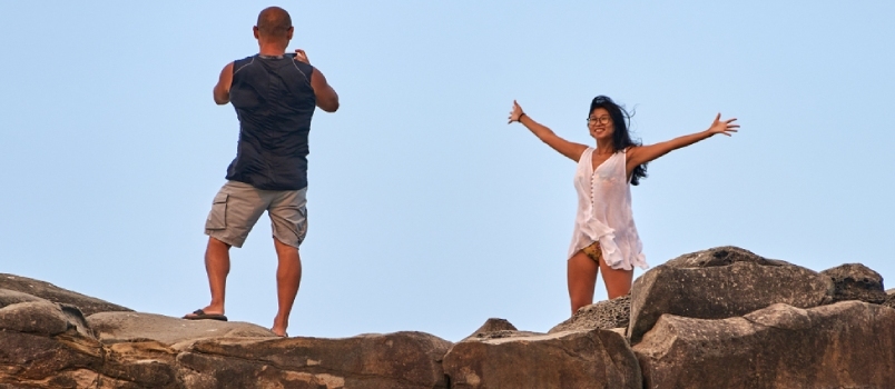 Una mujer posa alegremente con los brazos extendidos mientras su pareja le toma una fotografía.