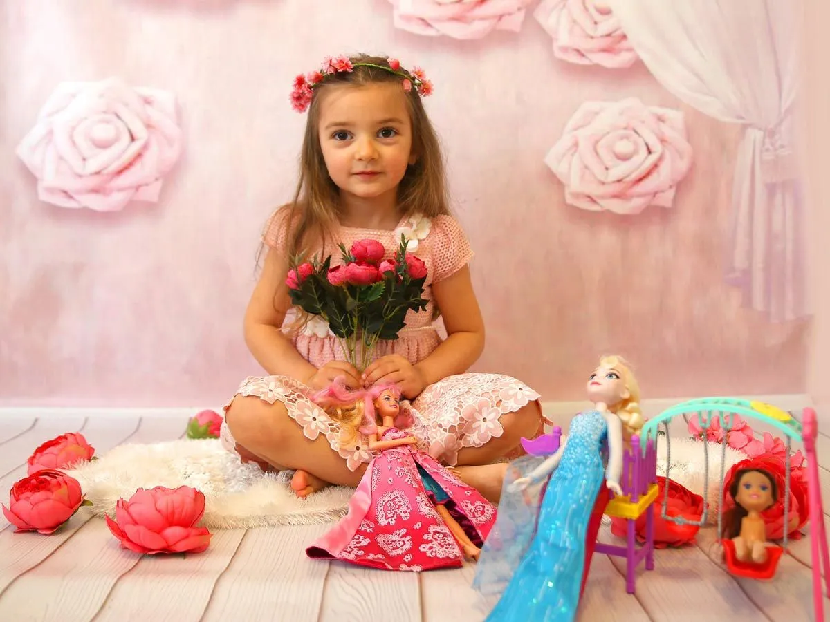Liten jente kledd som en rosa prinsesse satt på gulvet i et rosa rom med Barbie-dukkene sine.