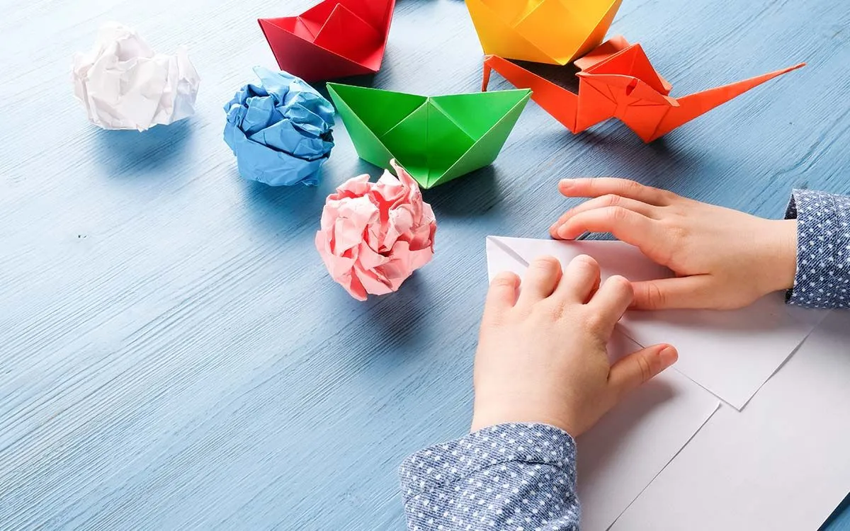 Nærbilde av hender som bretter papir som lager origamidyr. 