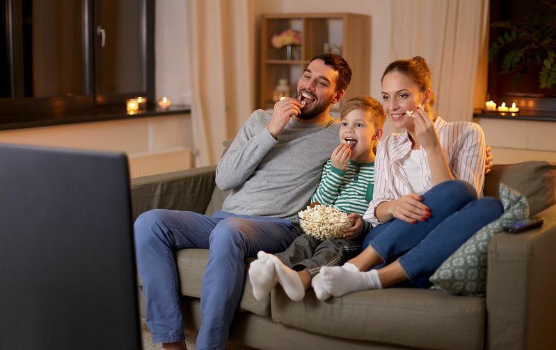 Šťastná rodina pozerá televíziu a jedia popcorn doma v noci