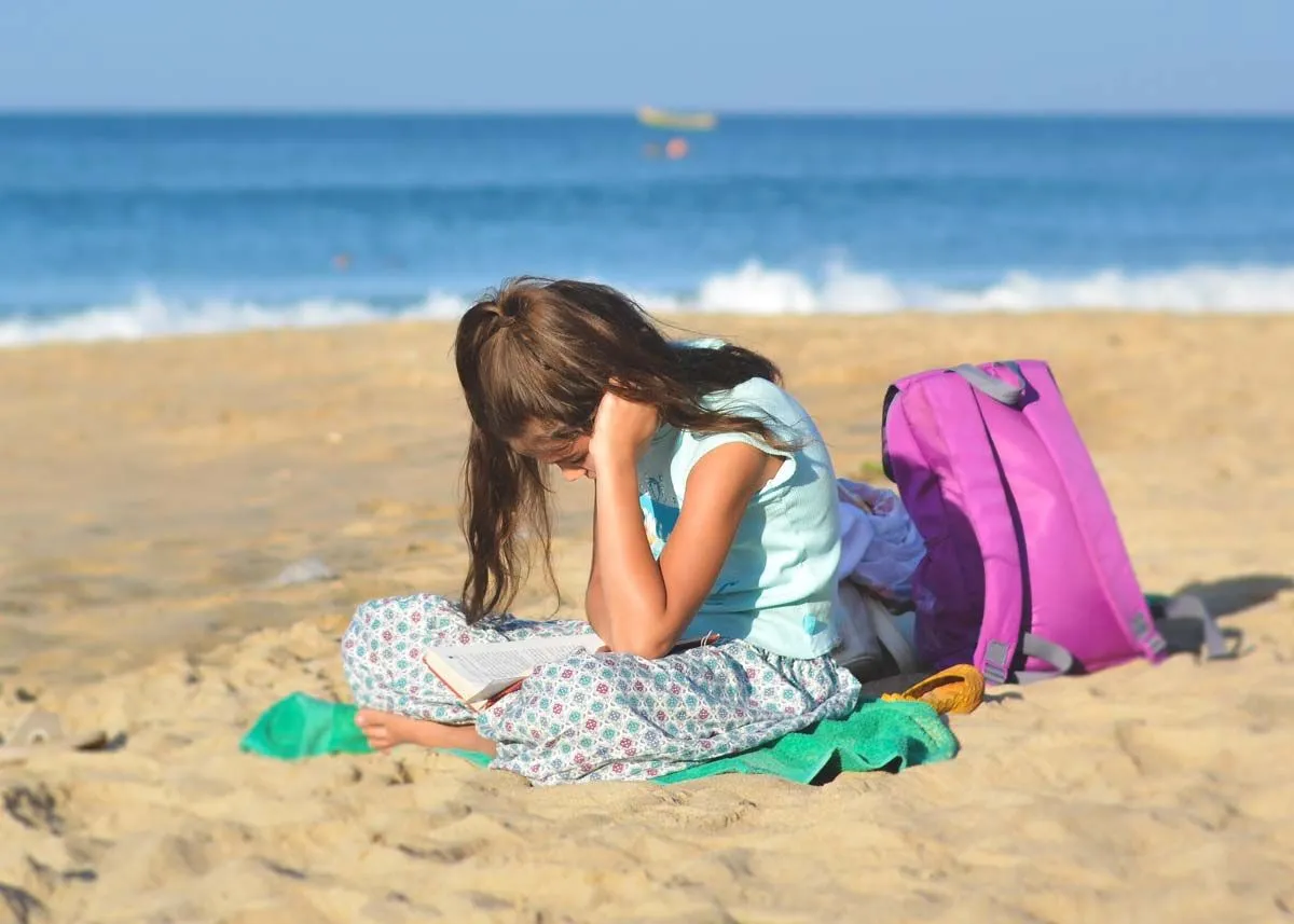 Liten jente satt i sanden på stranden og leste boken sin.