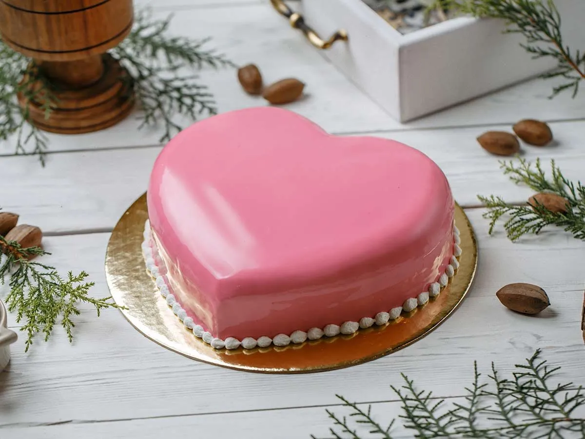 Рожевий торт у формі серця на дошці золотого торта.