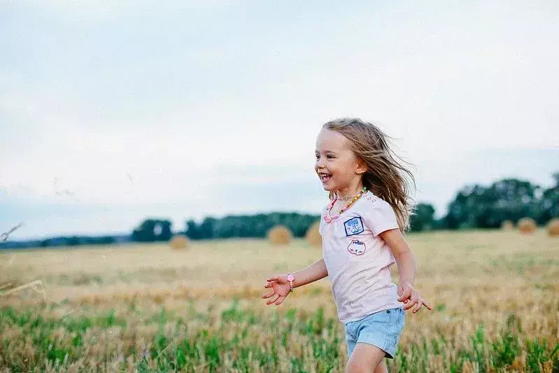 Малко момиченце се смее, докато бяга през поле с култури.