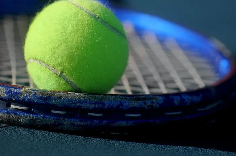 Nærbilde av en tennisball på strengene til en blå tennisracket.y