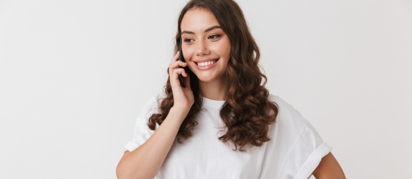Portrét usmívající se mladé neformální bruneta žena mluví na mobilním telefonu izolovaných na bílém pozadí