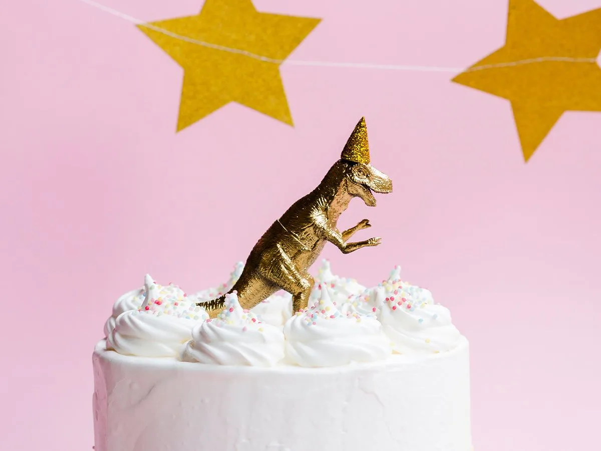 Hvit kake med en gull dinosaur lekemodell på toppen.