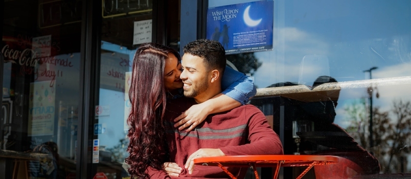 Moteris dieną lauko kavinėje bučiuoja vyro skruostą
