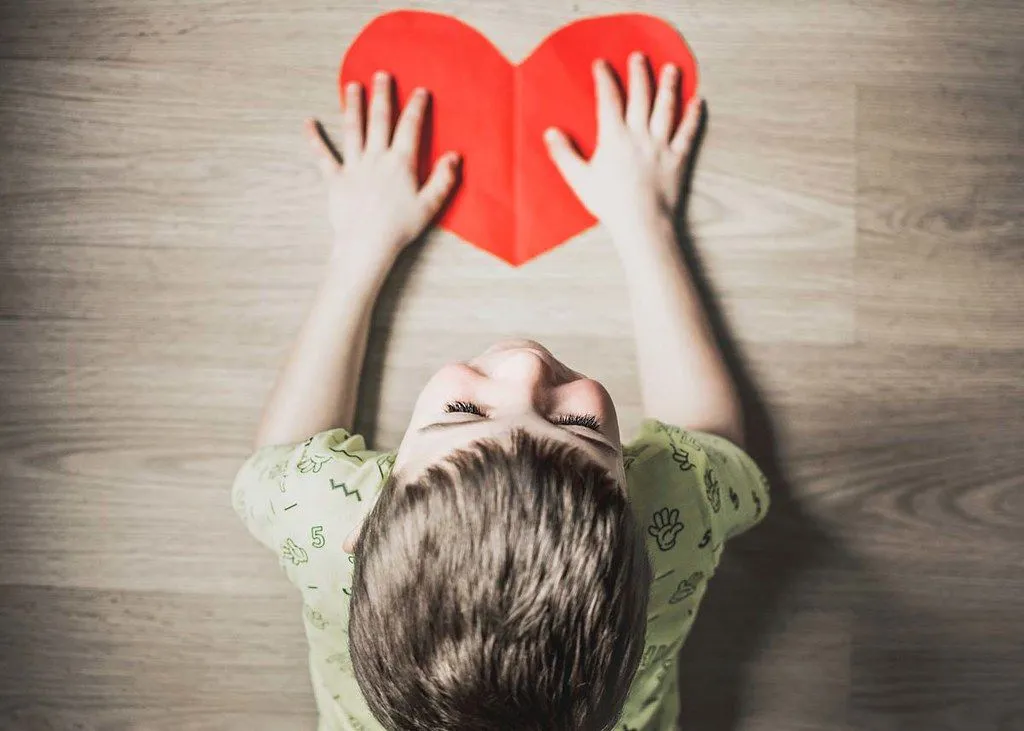 Et bilde ovenfra av en liten gutt som holder et rødt hjerte kuttet ut av papp.
