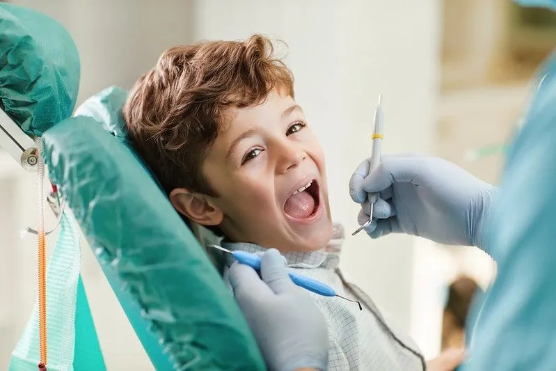 Glad gutt hos tannlegen sitter i stolen med åpen munn.
