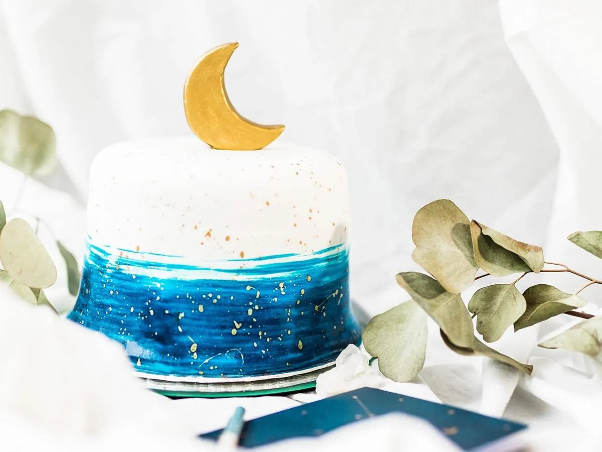 Bílý dort s modrou polevou natřenou kolem základny, zlatým půlměsícem nahoře a zlatou polevou.