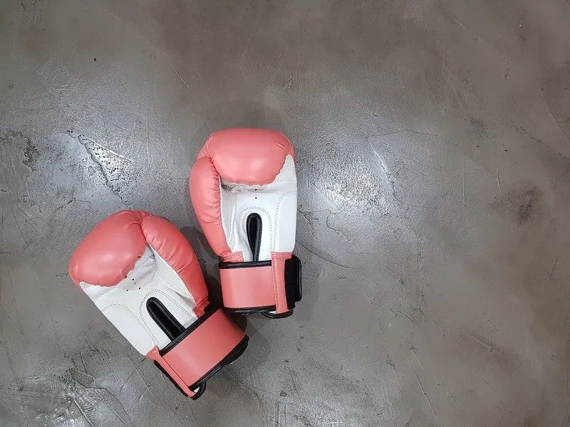 Et par rosa og hvite boksehansker på gulvet i treningsstudioet.
