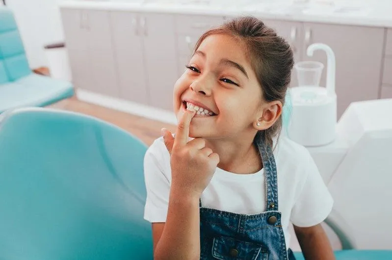 Ung jente hos tannlegen smiler og peker på tennene.