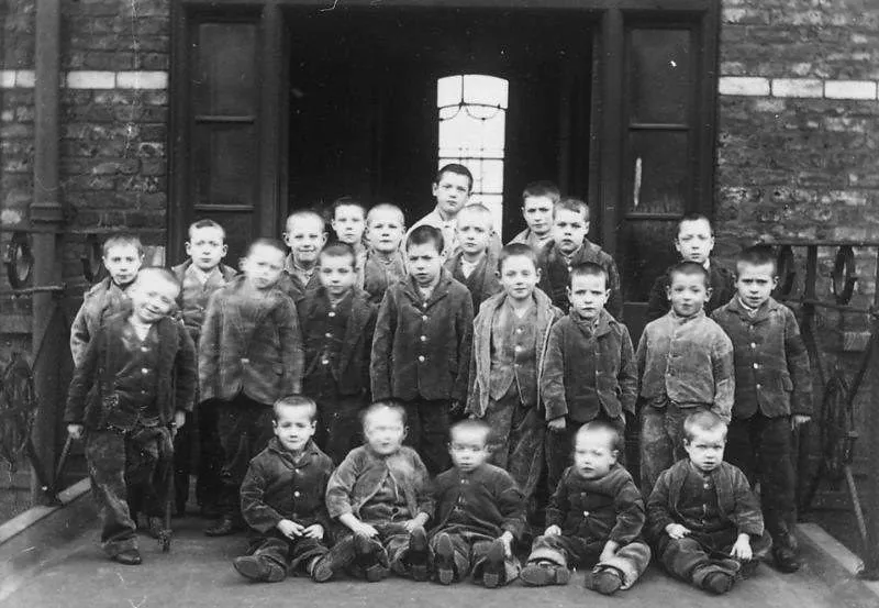 ვიქტორიანული სამუშაო სახლის წინ მდგომი ბავშვების შავ-თეთრი ფოტო.