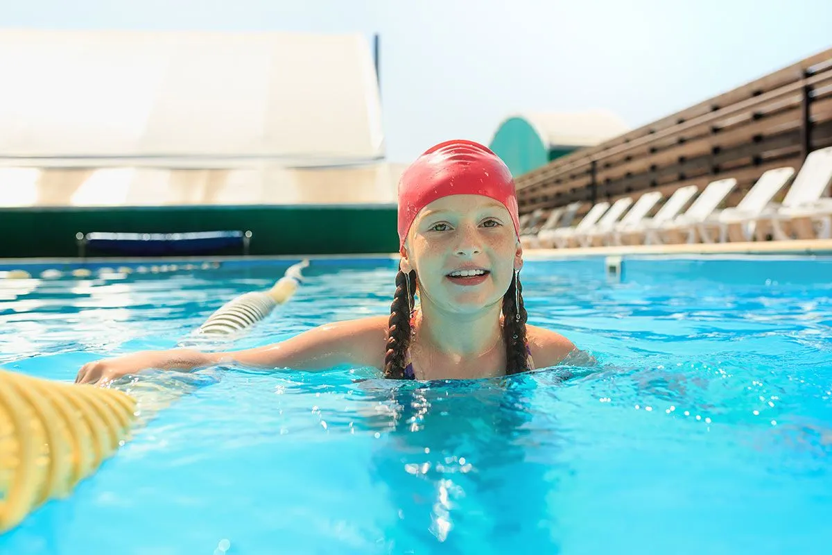 Ung pige, iført en rød badehætte, svømning i en udendørs pool.