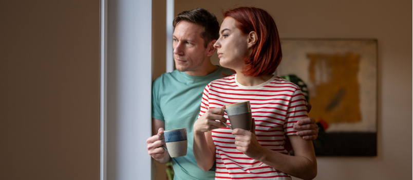 Pasangan berdiri di samping jendela sambil minum kopi 