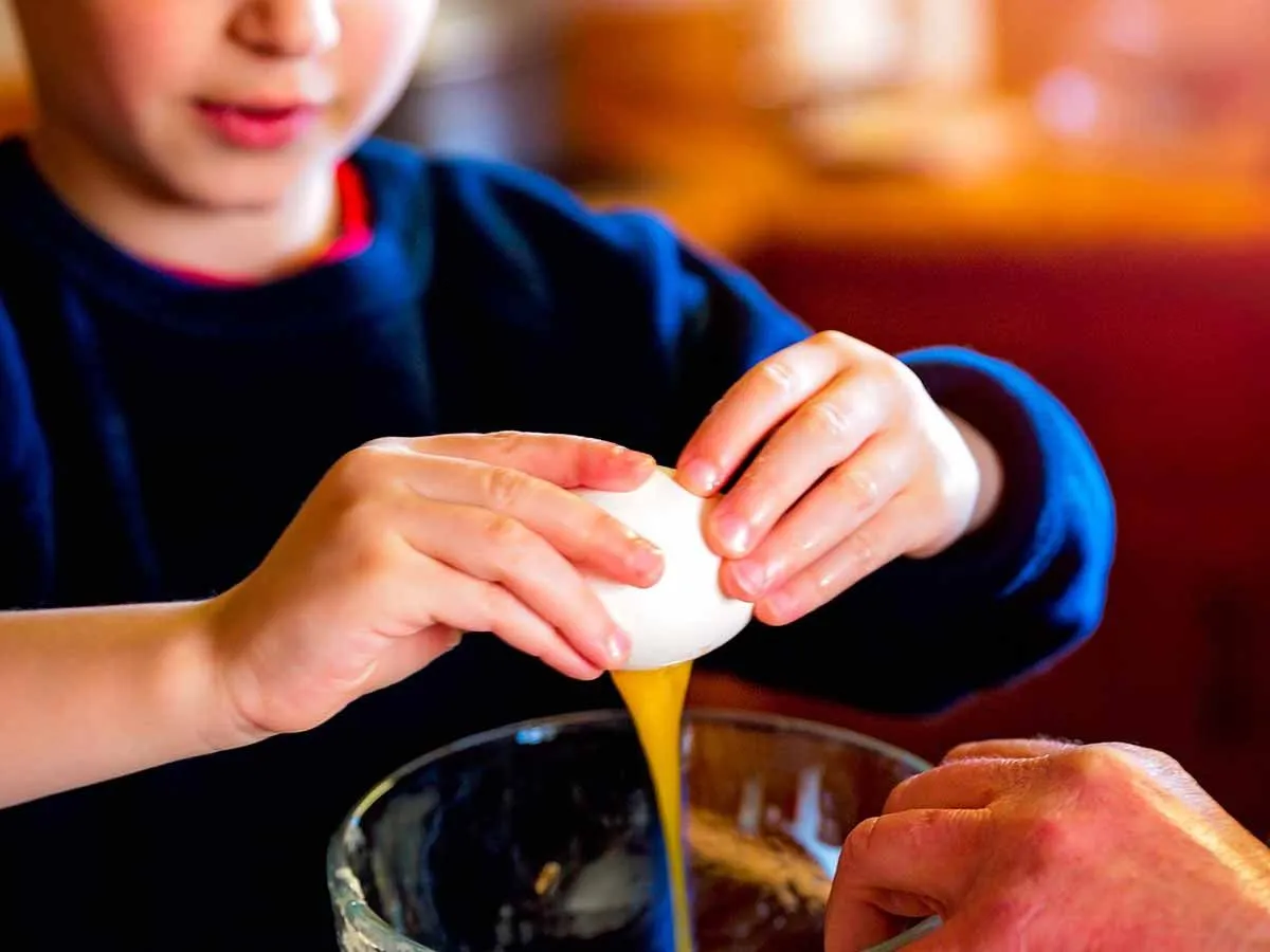 Närbild av en pojke som knäcker ett ägg i skålen med kakmix för att göra en pingvinkaka.