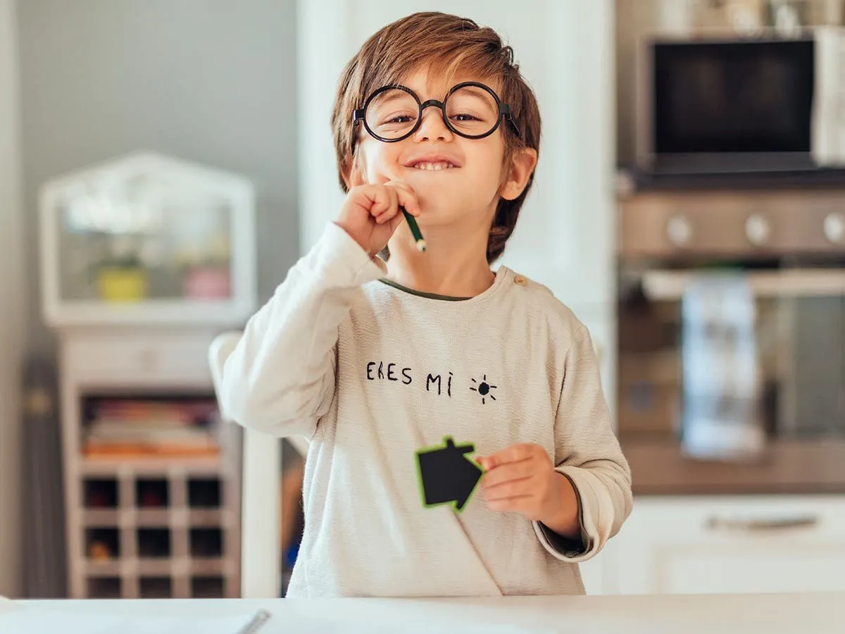 Un niño con gafas y sosteniendo un lápiz sonríe con orgullo a la cámara después de aprender a redondear números.