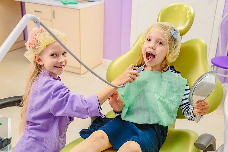 To små jenter leker tannlege som later som de bruker utstyret på hverandre.