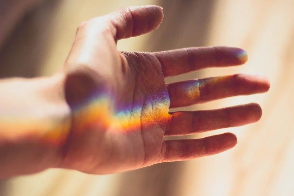 En hånd holdt frem med en regnbue av brutt lys på.