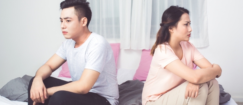 집에서 소파에 연달아 앉아 있는 젊은 불행한 아시아 커플