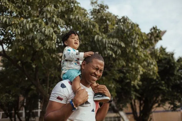Papà che porta il figlio sulle spalle, entrambi sorridono e ridono.