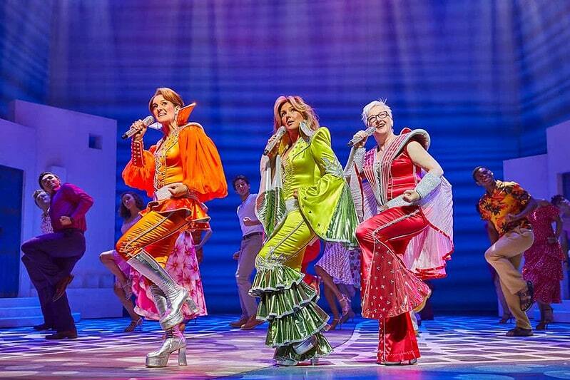 O elenco de Mamma Mia cantando uma música vestindo roupas brilhantes do ABBA.