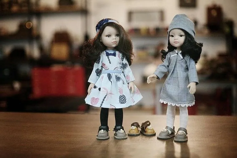 Duas bonecas com sapatos de couro sem cadarço, com um terceiro par no chão entre elas.
