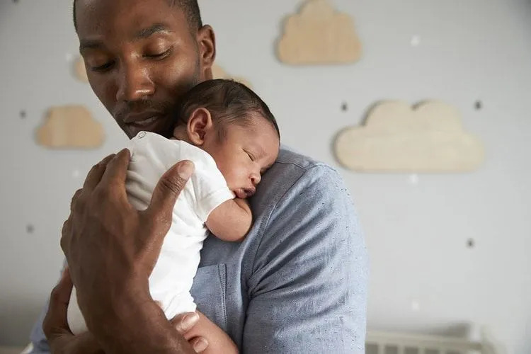 Tatăl își ține copilul nou-născut adormit în brațe