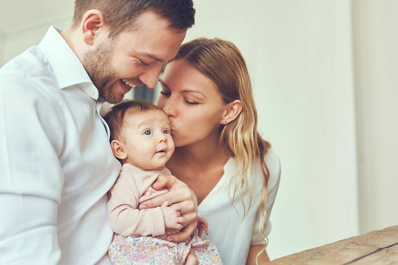 Nasmejana mati in oče doma držita svojo novorojeno hčerko