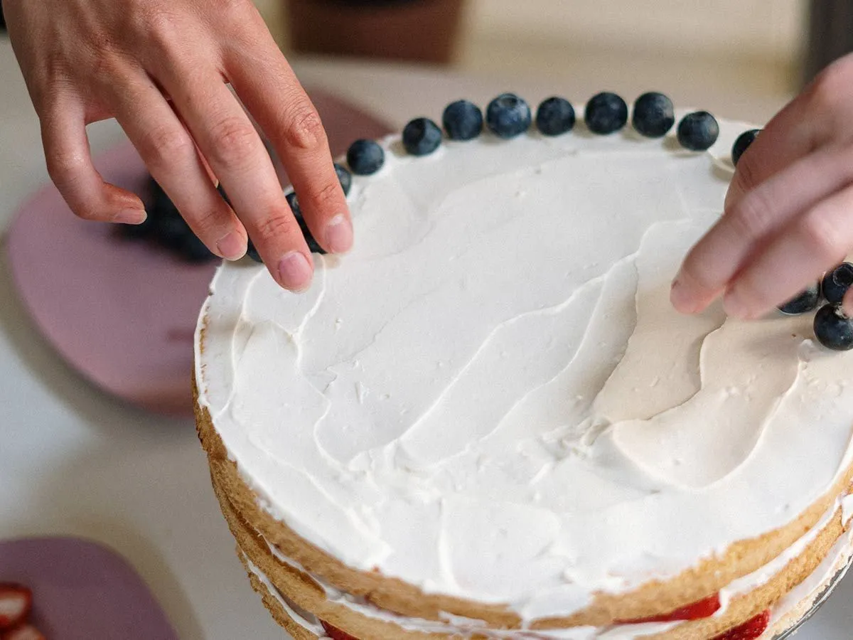 Asmuo, puošiantis ledinį pyragą su mėlynėmis ant viršaus.
