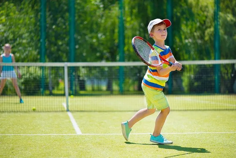 Ung gutt i en fargerik stripete t-skjorte og caps spiller tennis.