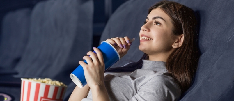 Jonge aantrekkelijke vrouw kijken naar een film in de bioscoop glimlachend en nippen aan haar drankje Copyspace Entertainment