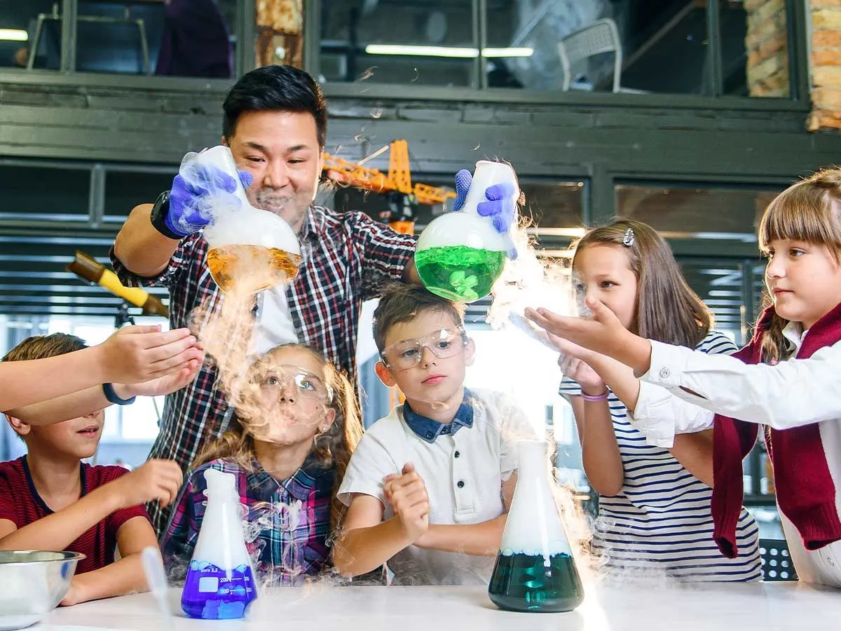 Insegnante che mostra ai bambini esperimenti scientifici con liquidi colorati in boccette.