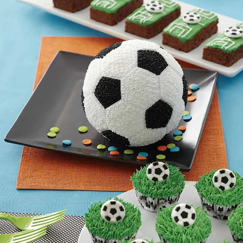 En fotbollstårta på en tallrik, några cupcakes dekorerade med grönt gräsglasyr och en islagd fotboll och brownies isade för att se ut som en fotbollsplan.