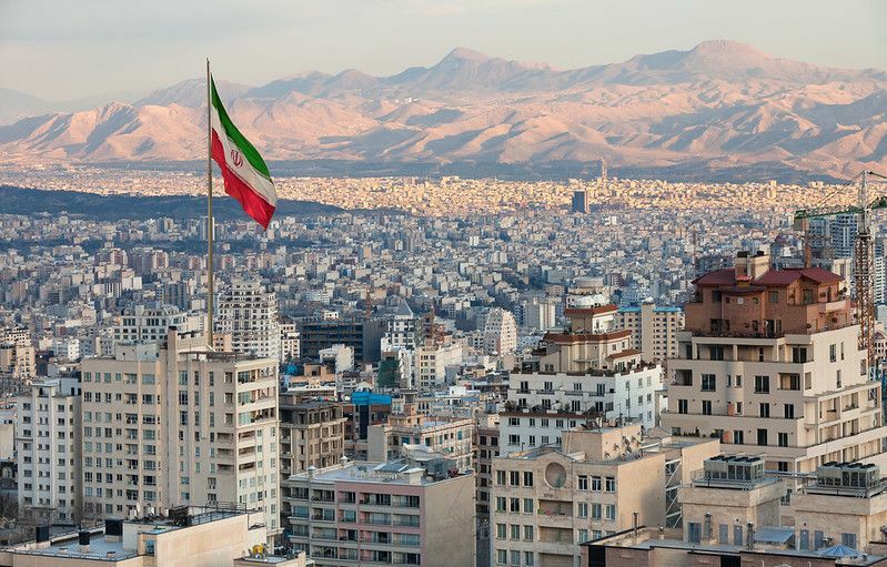 Viftar Irans flagga ovanför Teherans silhuett vid solnedgången