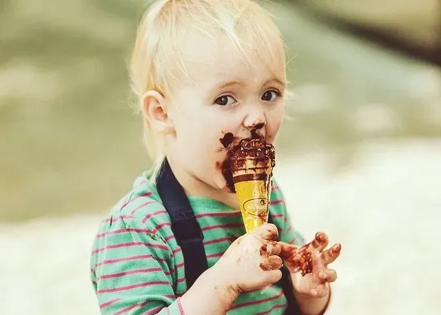 νεαρό ξανθό αγόρι που τρώει ακατάστατο παγωτό σοκολάτας