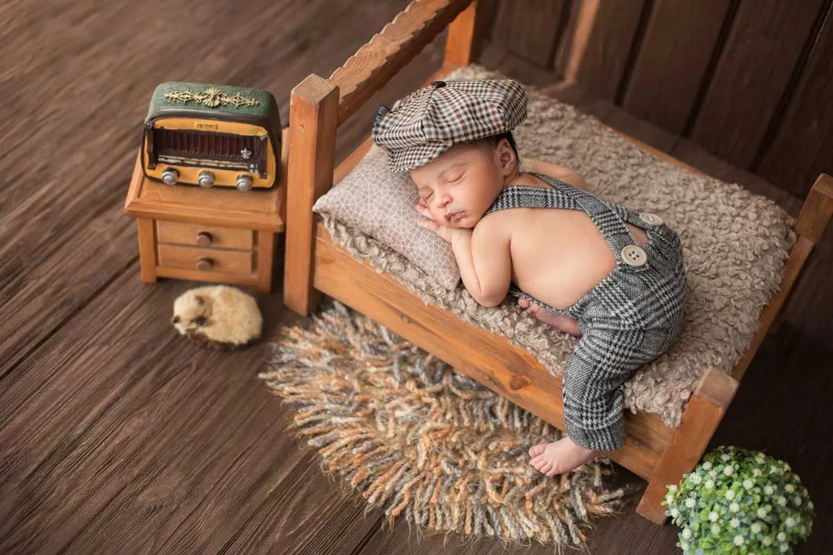 Chlapeček leží na přední straně, spí na miniaturní posteli a nosí kostkovaný klobouk.