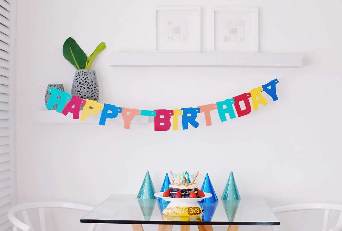 Su gimtadieniu parašyta ant sienos už stalo su tortu ir vakarėlių kepuraitėmis kabantoje reklaminėje juostoje.