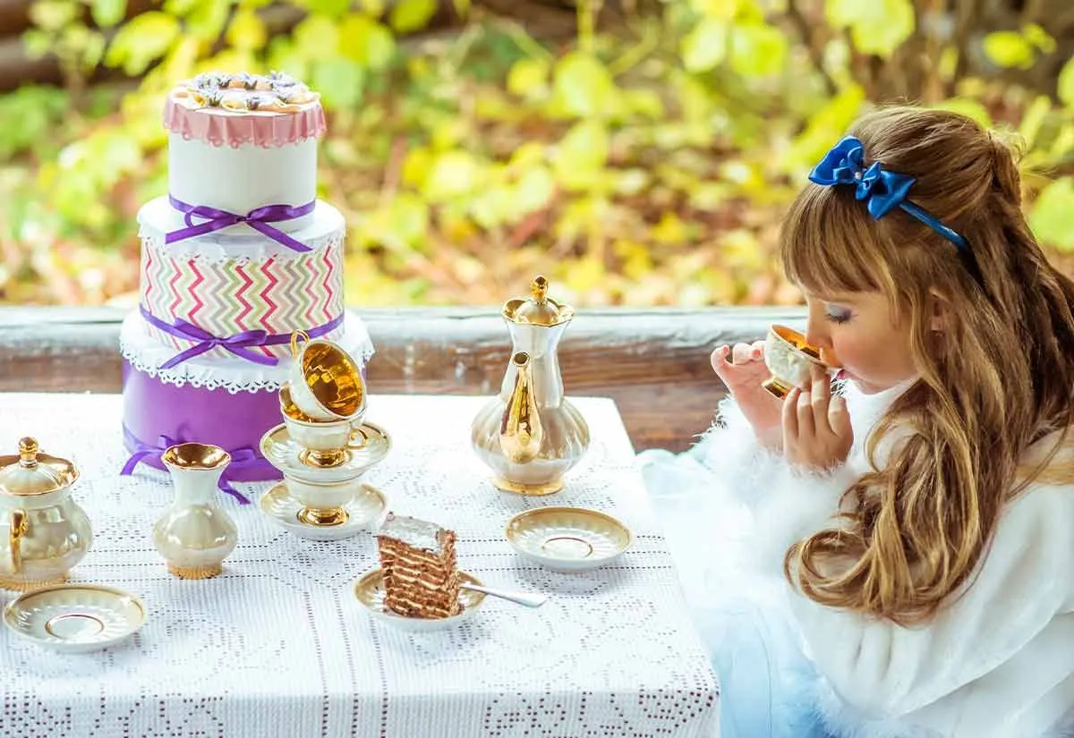 Маленька дівчинка сиділа за столом на чаювання Божевільного Капелюшника з триярусним тортом.