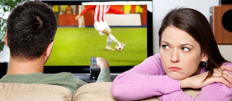 Bilde av kvinne som kjeder seg mens partneren hennes ser på sport Jeg er forfatteren av bildet på TV-skjermen