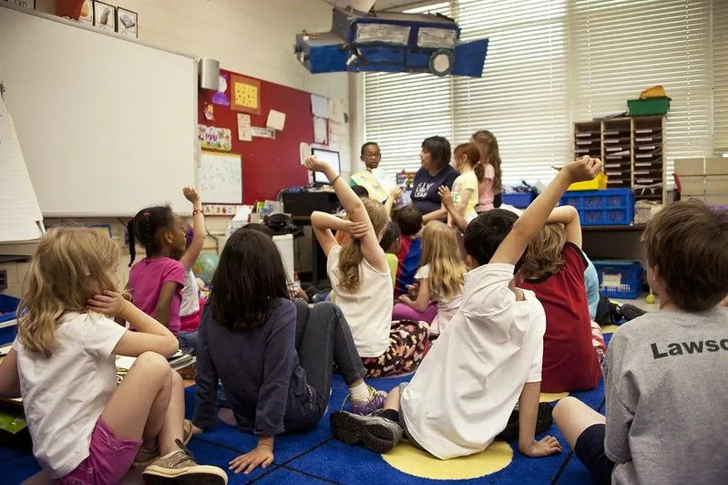 Klasserom med barn som rekker opp hånden og sitter på gulvet.