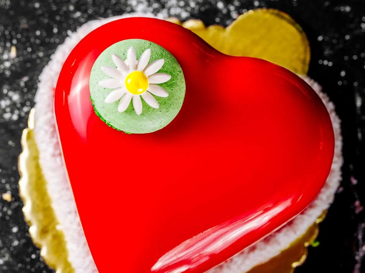 Червоний пиріг у формі серця із зеленим макаруном з ромашкою на вершині, на вершині торта.
