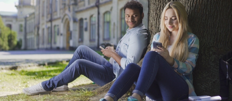 Férfi mobiltelefon ül a fa alatt, és nézi a lányt használ telefont