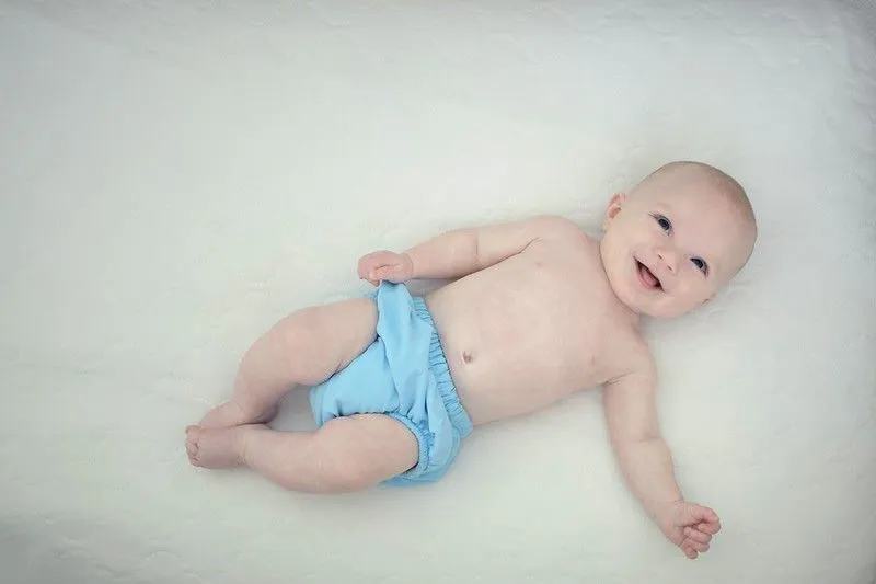 En baby med blå bleie smiler til kameraet.