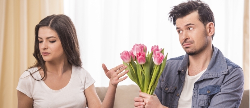 집에 있는 화난 여자친구에게 꽃 다발을 선물하고 있는 청년