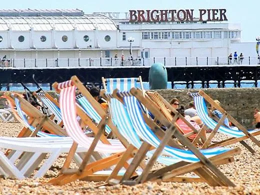 Lehátka na břehu Brighton Beach s Brighton Pier v pozadí