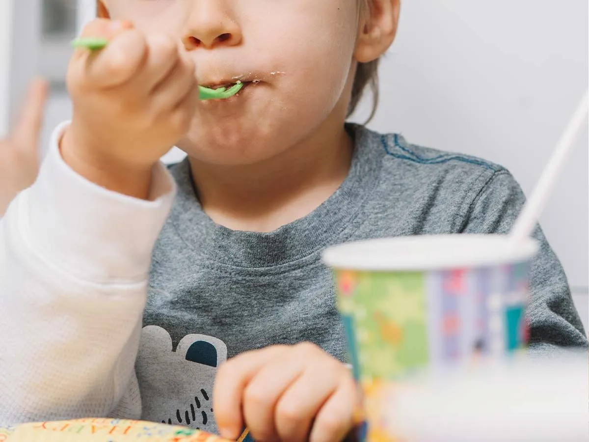 Nærbilde av en ung gutt som spiser en bit av Toy Story-kake på en grønn plastgaffel.