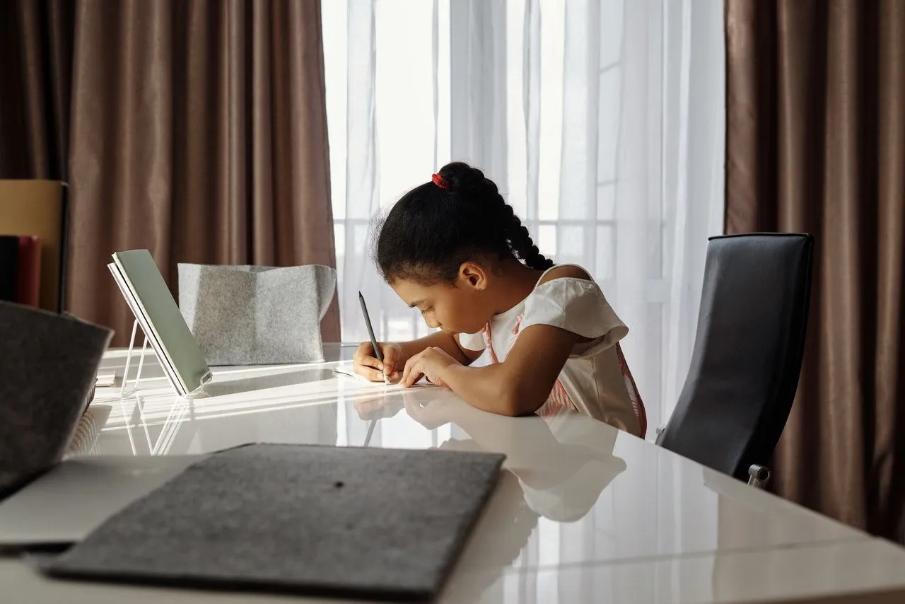 Jauna mergina sėdi prie savo stalo, rašo ir praktikuojasi naudodama idiomas.