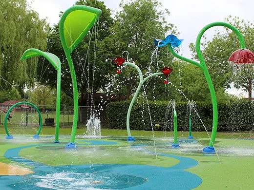 उष्णकटिबंधीय स्प्रिंकलर और रंगीन पानी के जेट के साथ पार्क में स्पलैश पैड