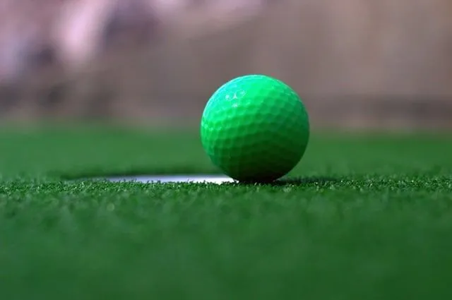 Nærbilde av en grønn golfball på kanten av hullet på golfbanen.